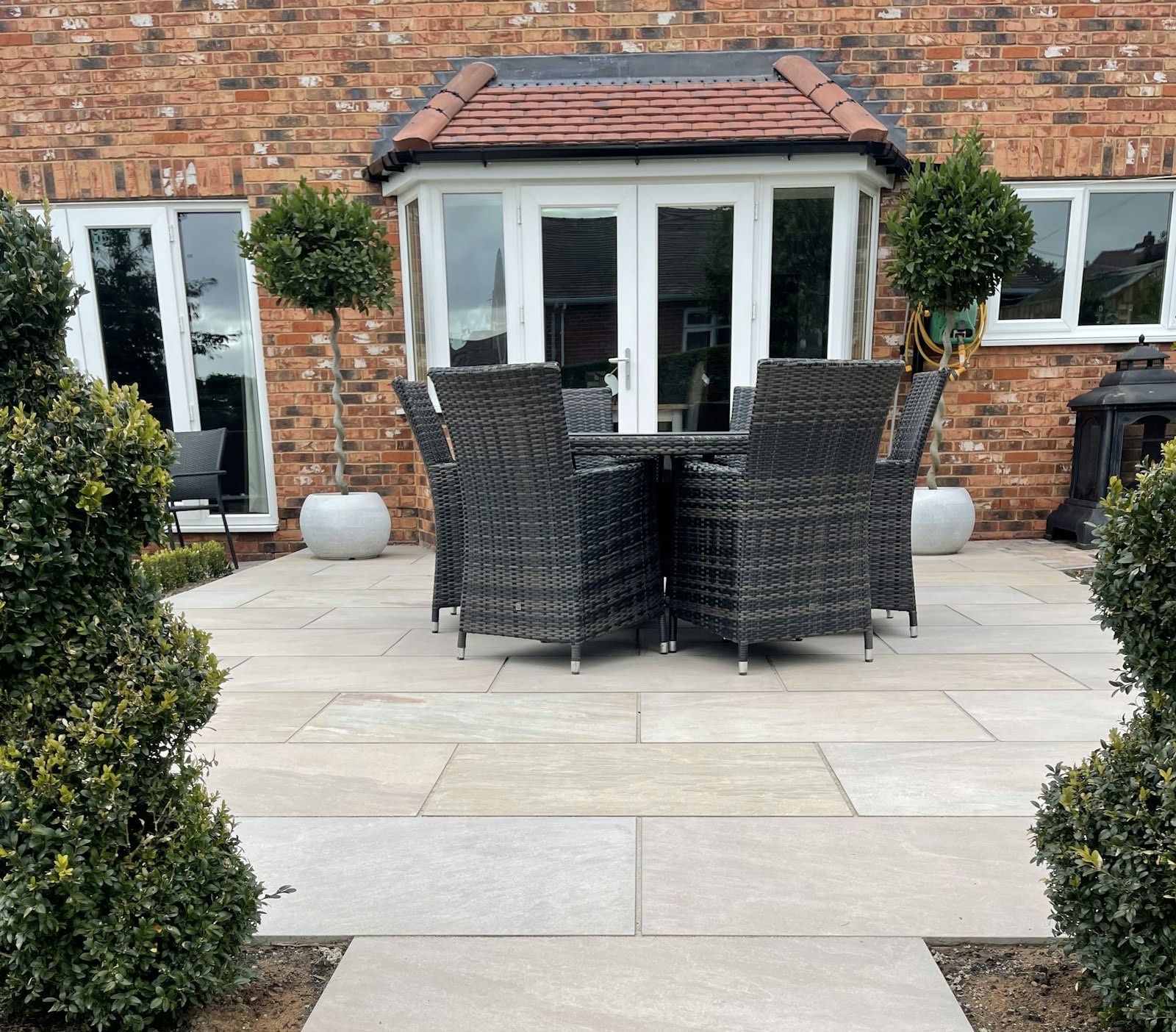 A newly laid pale stone patio with outdoor dining set beside a brick house